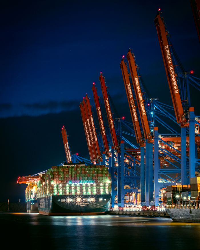 A large container ship docked at Hamburg's port, illuminated against the night sky.